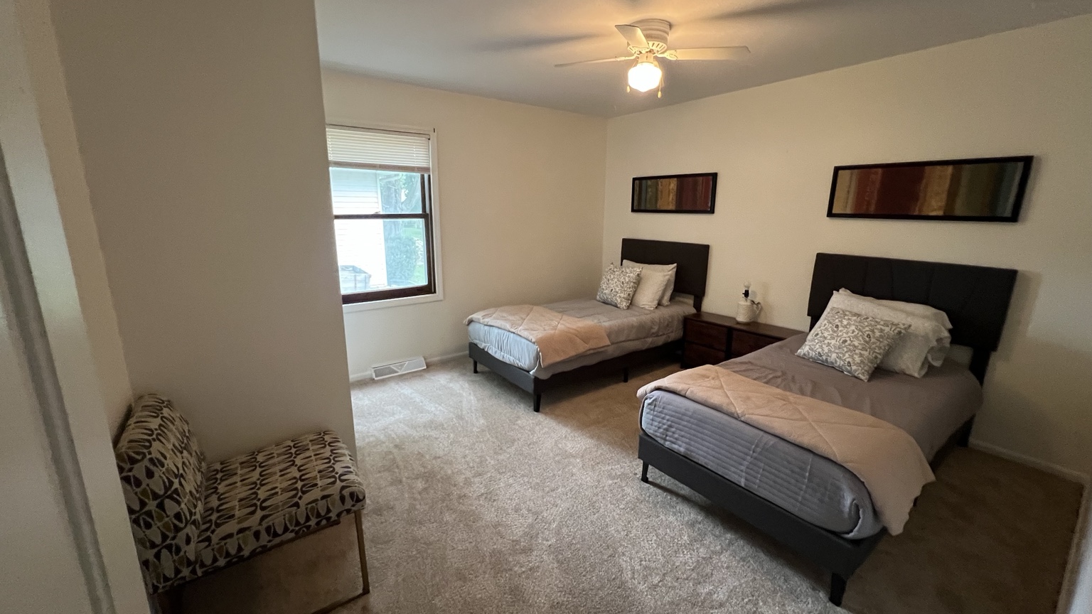 Shared bedroom with two gray beds, coordinated artwork, and a sitting chair